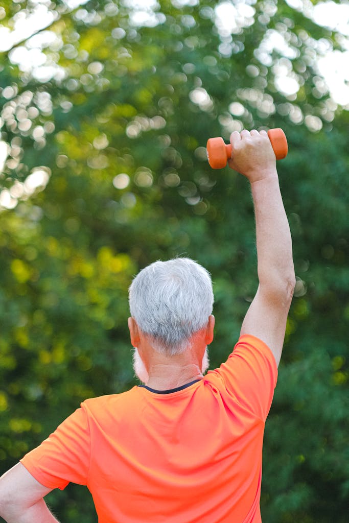 Back view of a senior man lifting a dumbbell outdoors, promoting fitness and vitality.