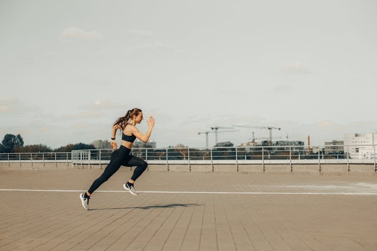 Woman sprinting on a rooftop in athletic wear during the day.