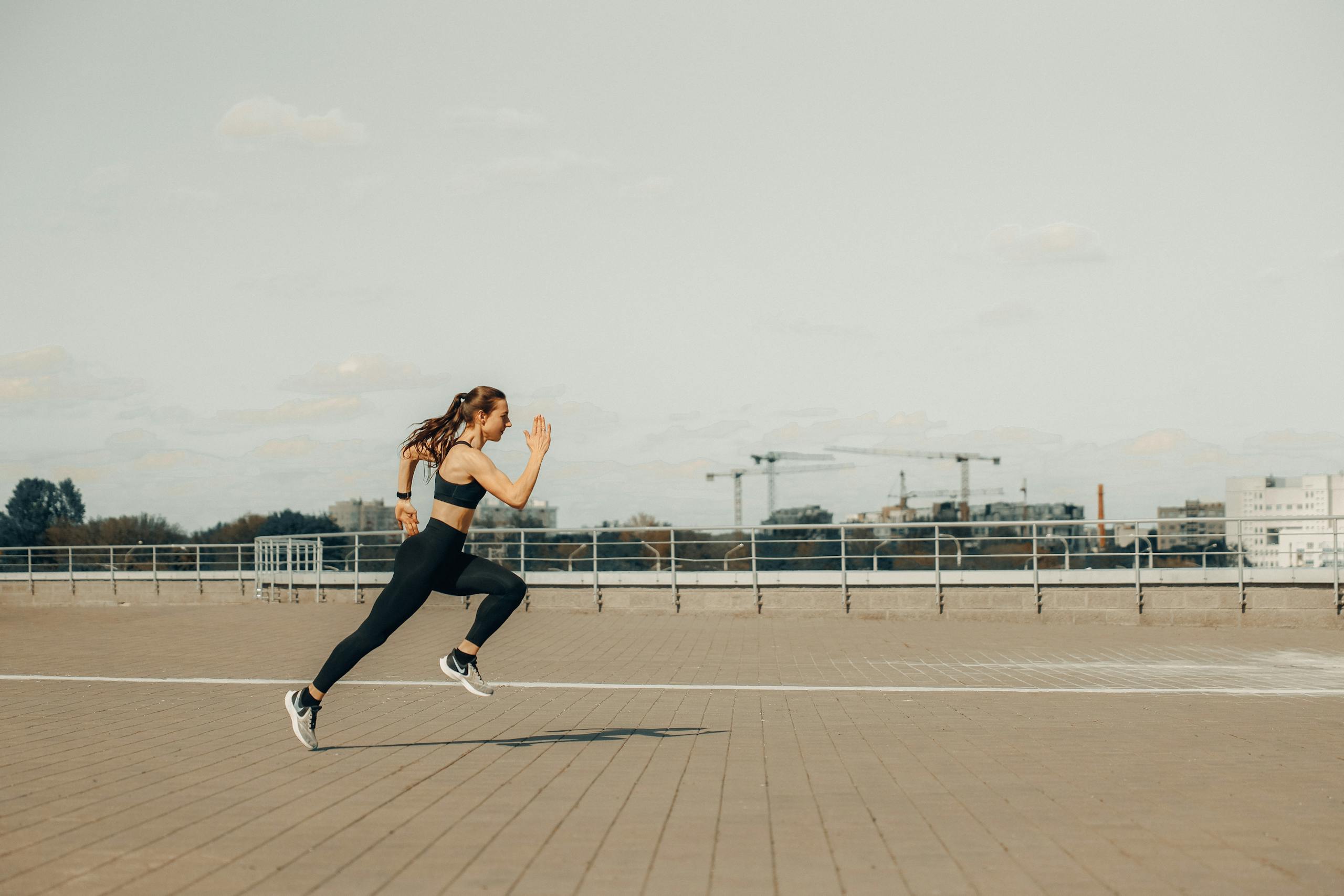 Woman sprinting on a rooftop in athletic wear during the day.